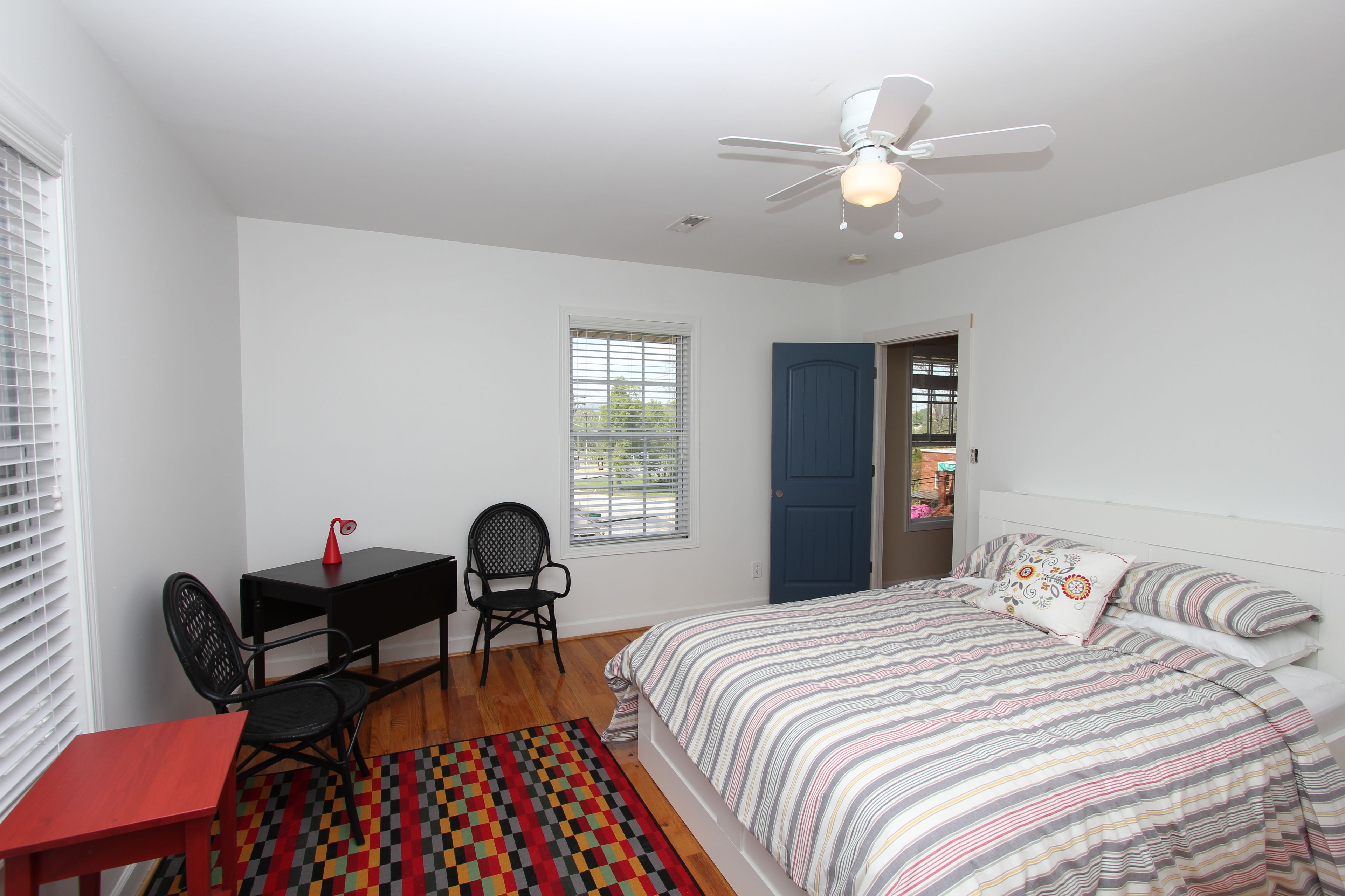 Une chambre à coucher comprenant un lit, un bureau, une chaise, un ventilateur de plafond et une fenêtre.