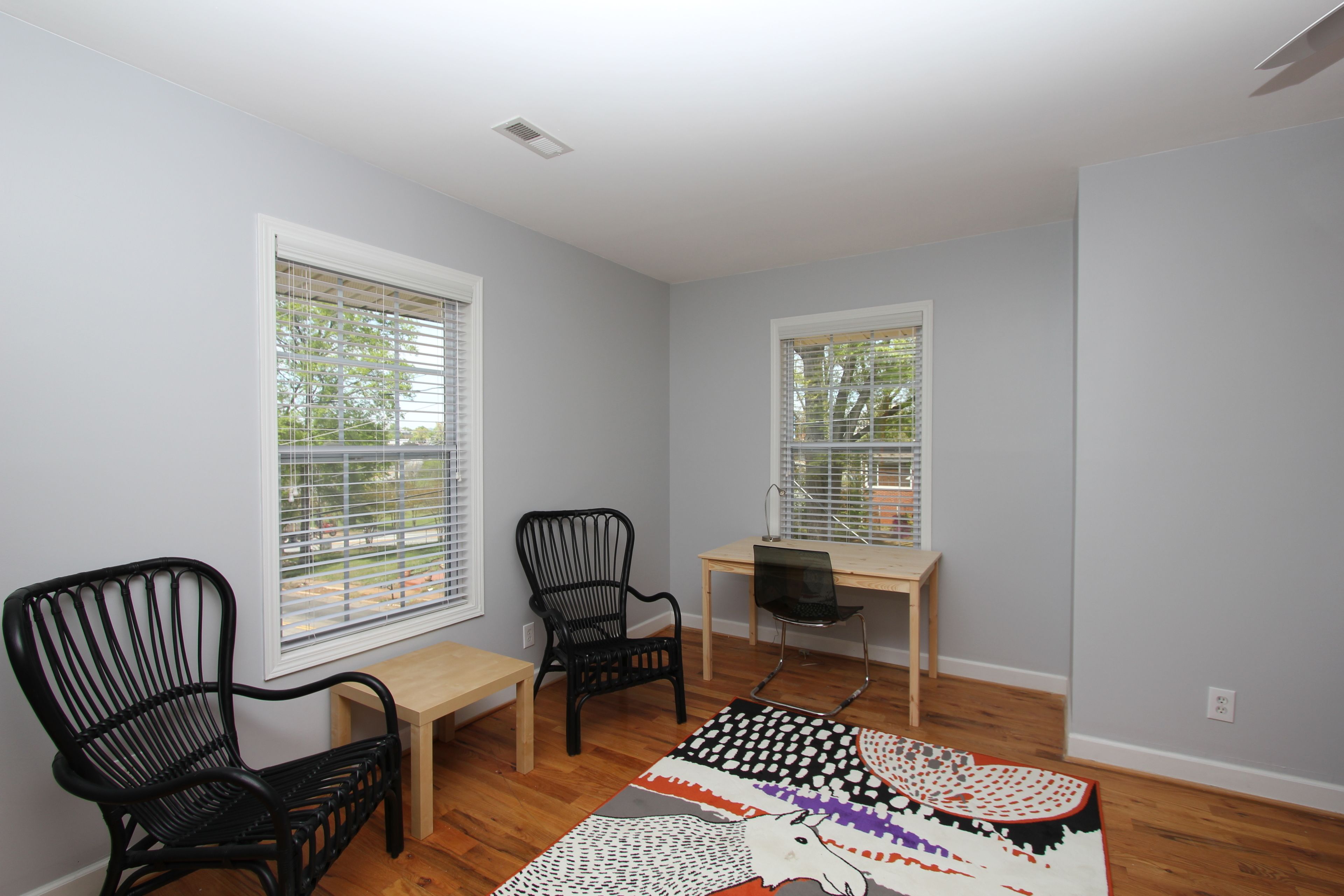 A room with two black chairs, a wooden table, and a laptop on a desk.