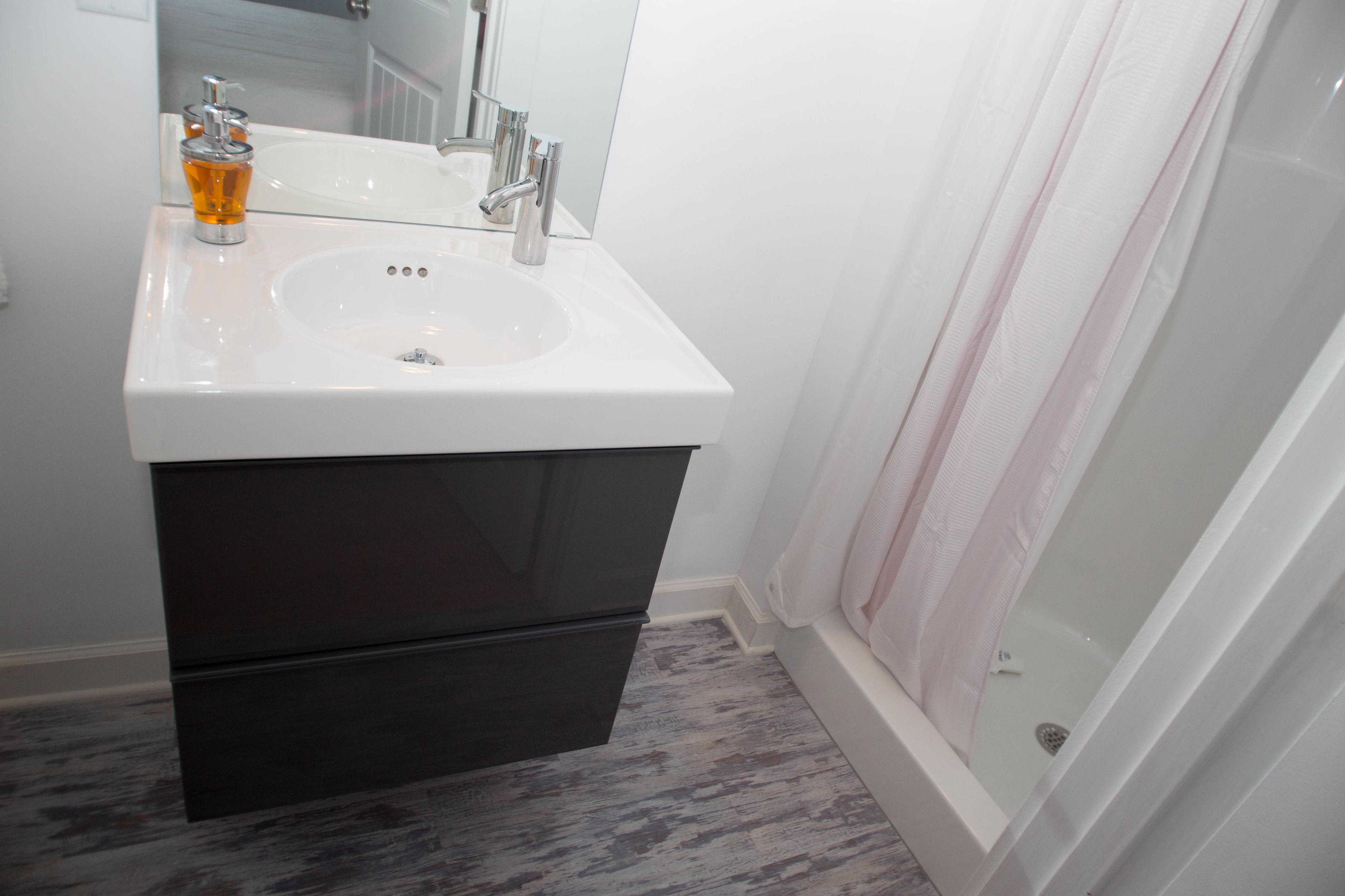 A bathroom with a white sink, dark cabinet, and a shower curtain.