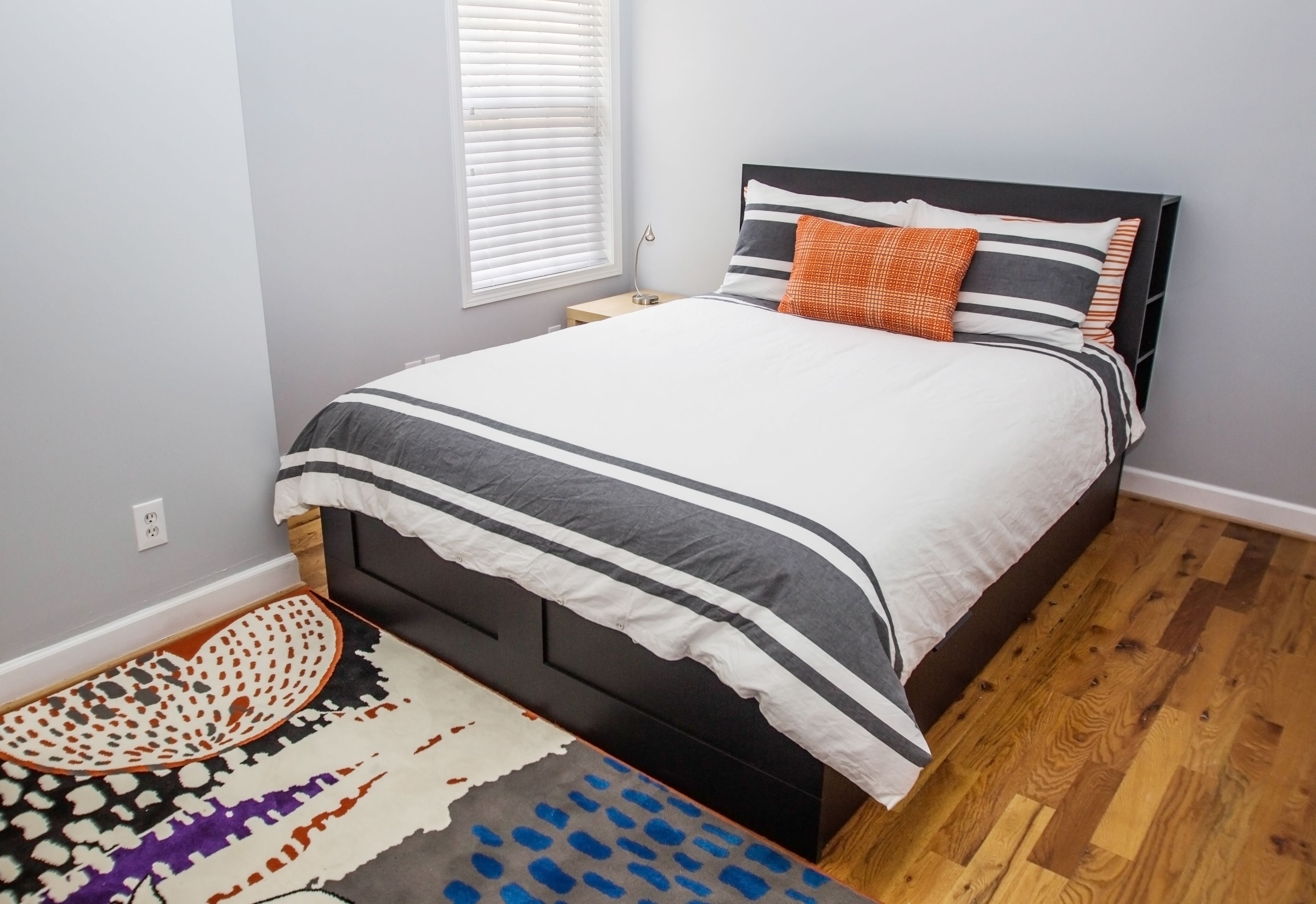 Un letto rifatto con ordine, con una coperta a righe e cuscini, un tappeto decorato e un pavimento in legno.