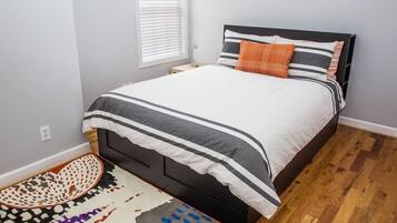 Un letto rifatto con ordine, con una coperta a righe e cuscini, un tappeto decorato e un pavimento in legno.