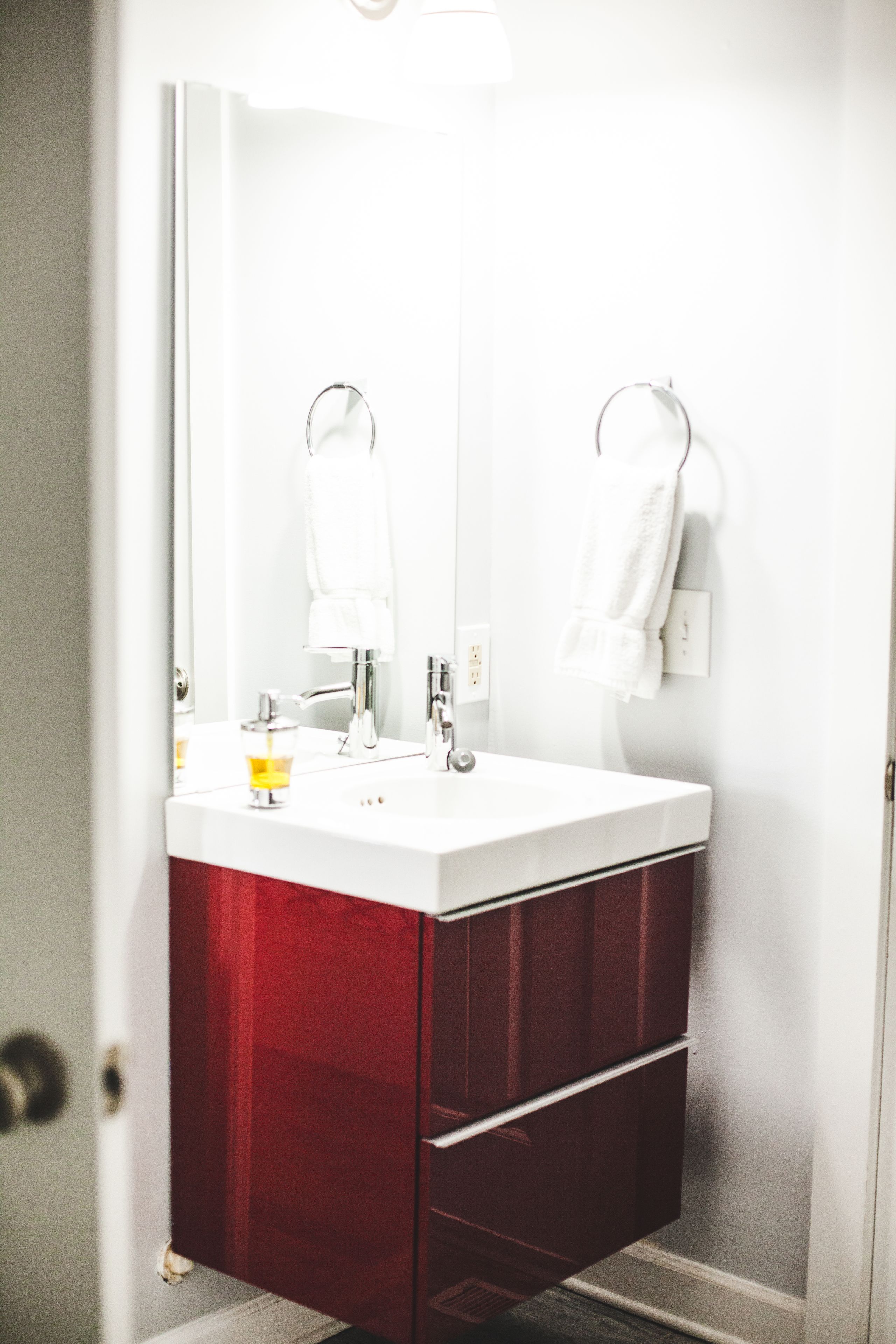 Un baño con lavamanos blanco, un espejo y un mueble rojo.