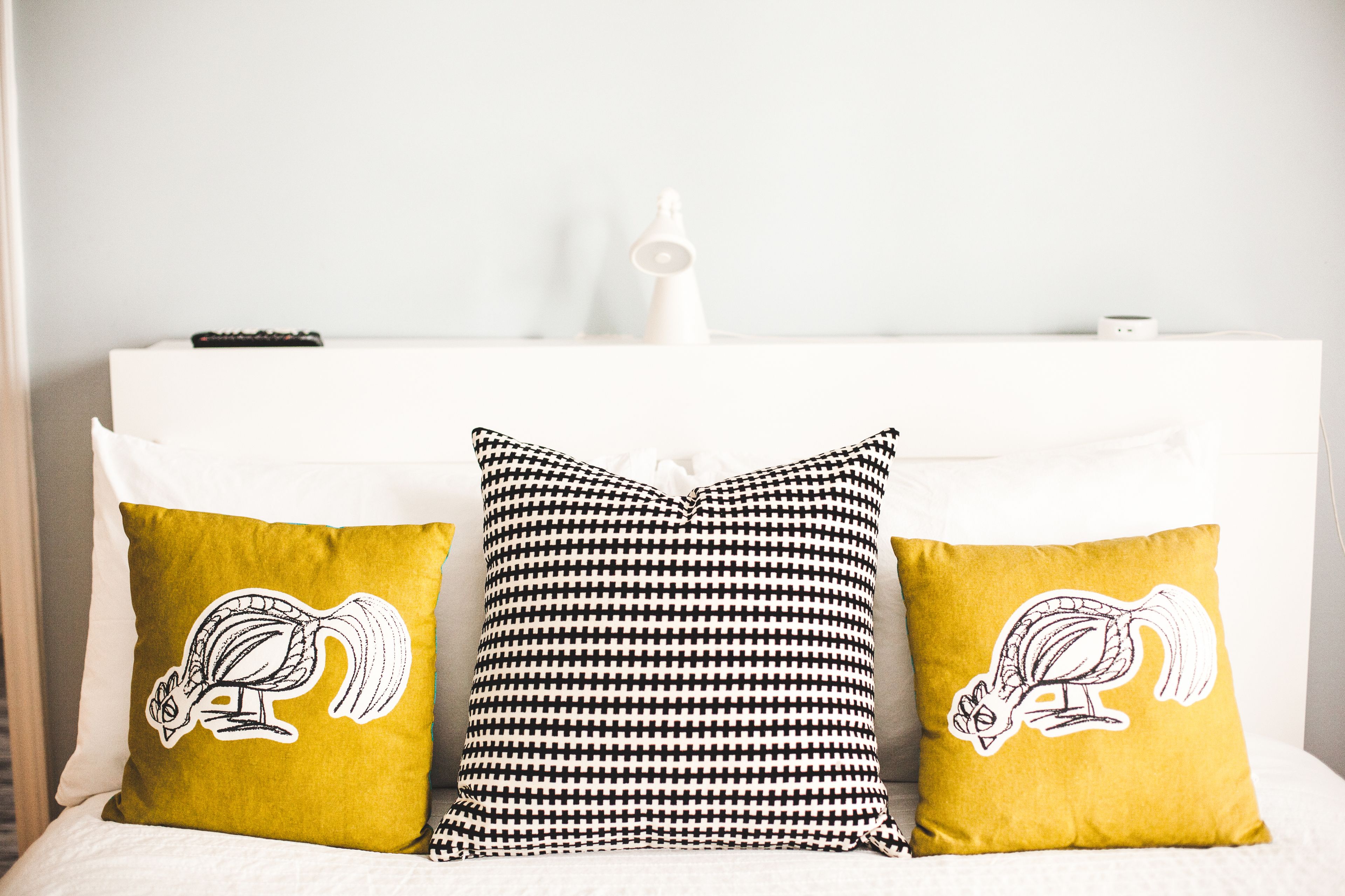 Un lit avec deux oreillers : un jaune et un autre noir et blanc à motifs, tous deux ornés d’un motif représentant un écureuil.