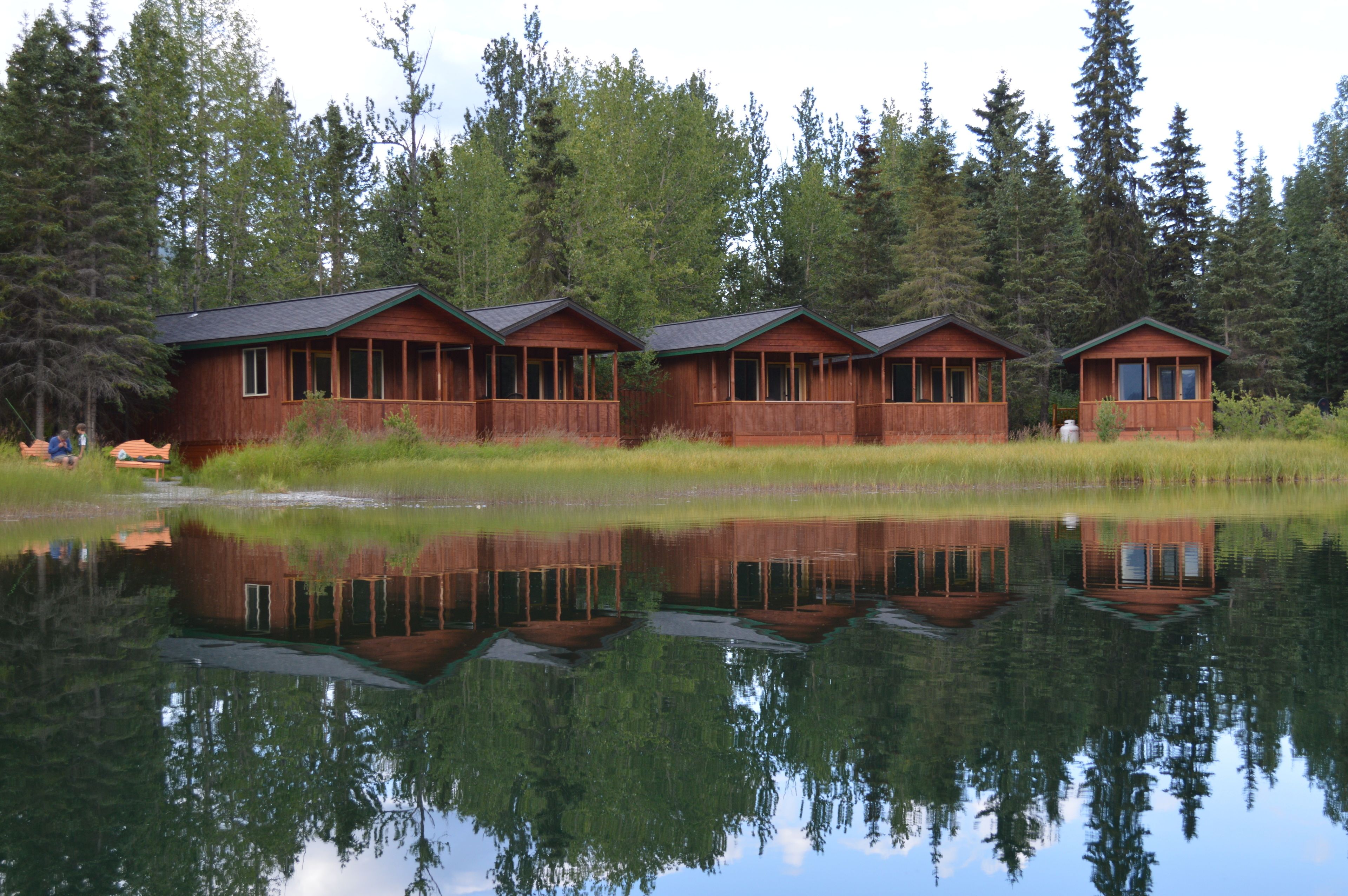 Rivi puisia mökkejä sijaitsee rauhallisen järven rannalla, ja niitä ympäröi tiheä metsä.