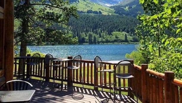 A wooden deck with outdoor seating overlooking a lake and mountains. - Summit Lake Lodge (Moose Pass)