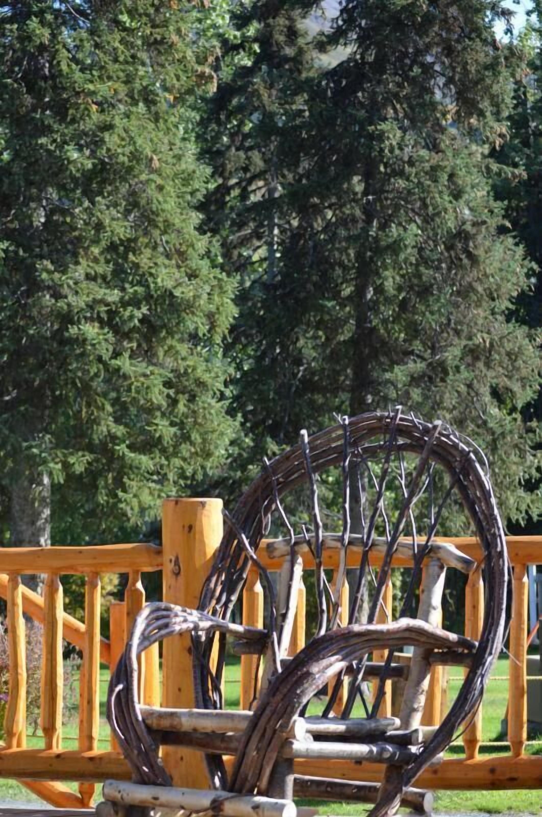 Une chaise en bois rustique, dotée d’un siège et d’un dossier en osier, est placée sur une terrasse en bois avec une rambarde jaune.