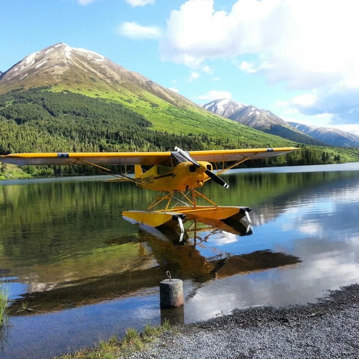 Ein gelbes Wasserflugzeug liegt auf einem ruhigen See, im Hintergrund Berge.