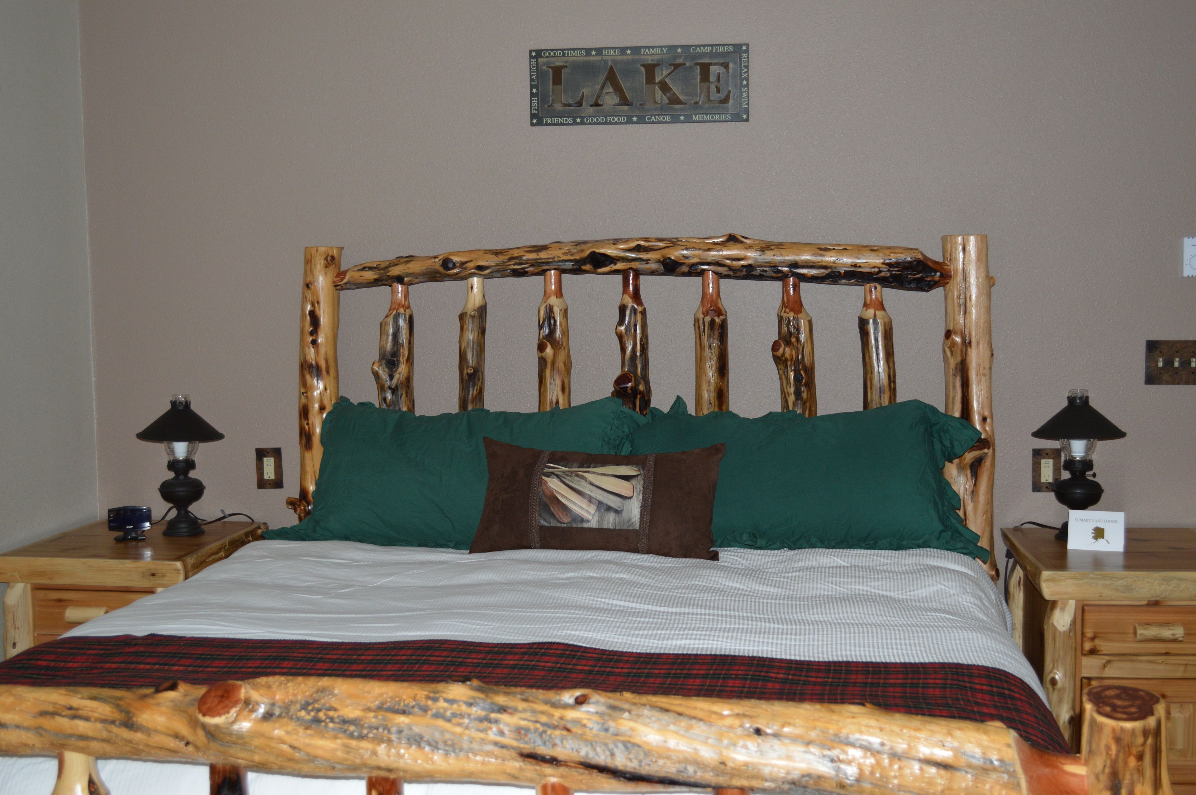 Ein Bett mit einem rustikalen Holz-Kopfstück, grünen Kissen und einer Karo-Decke.