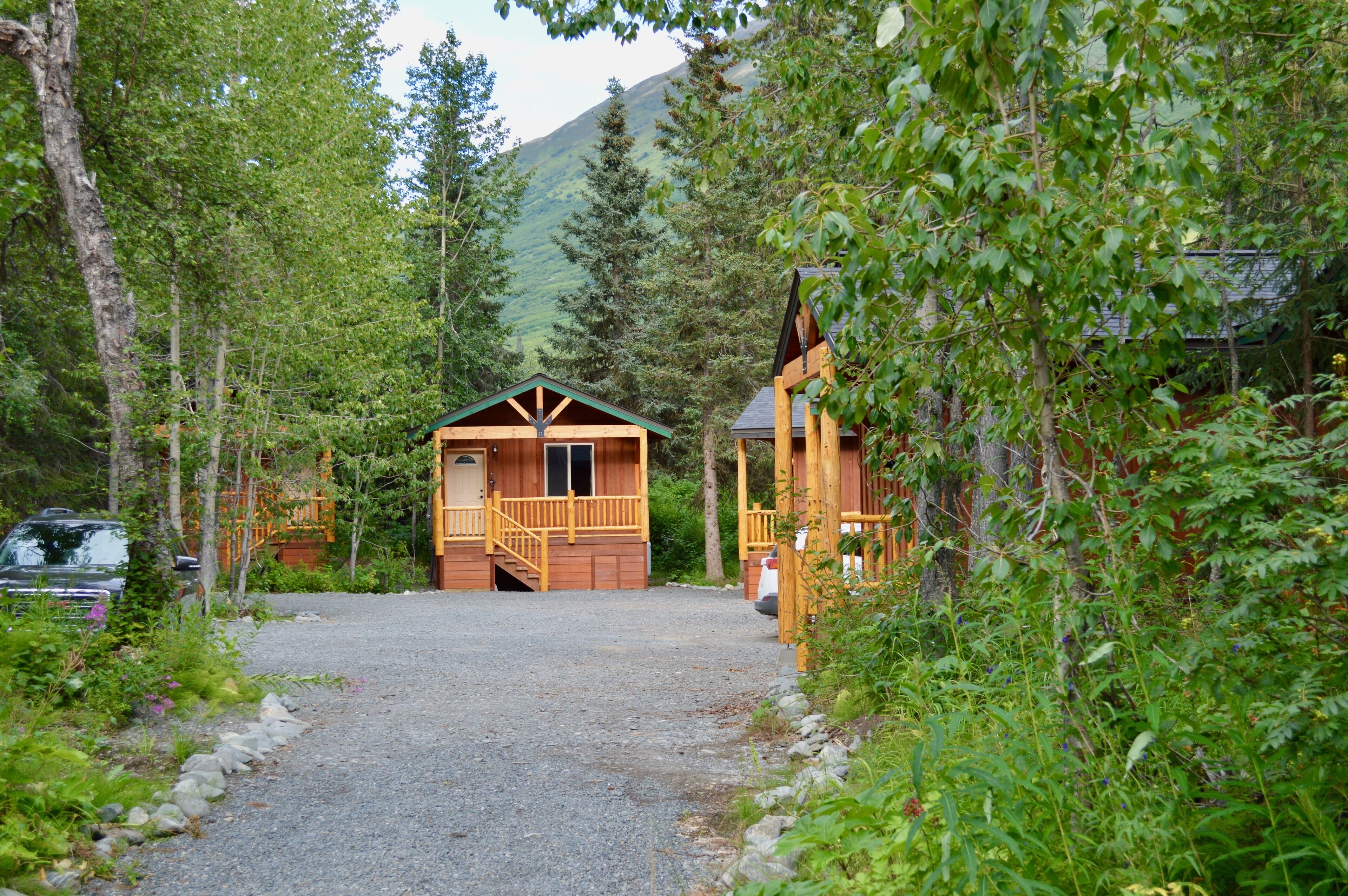A cabin with a front porch and a garage, surrounded by dense forest and mountains.