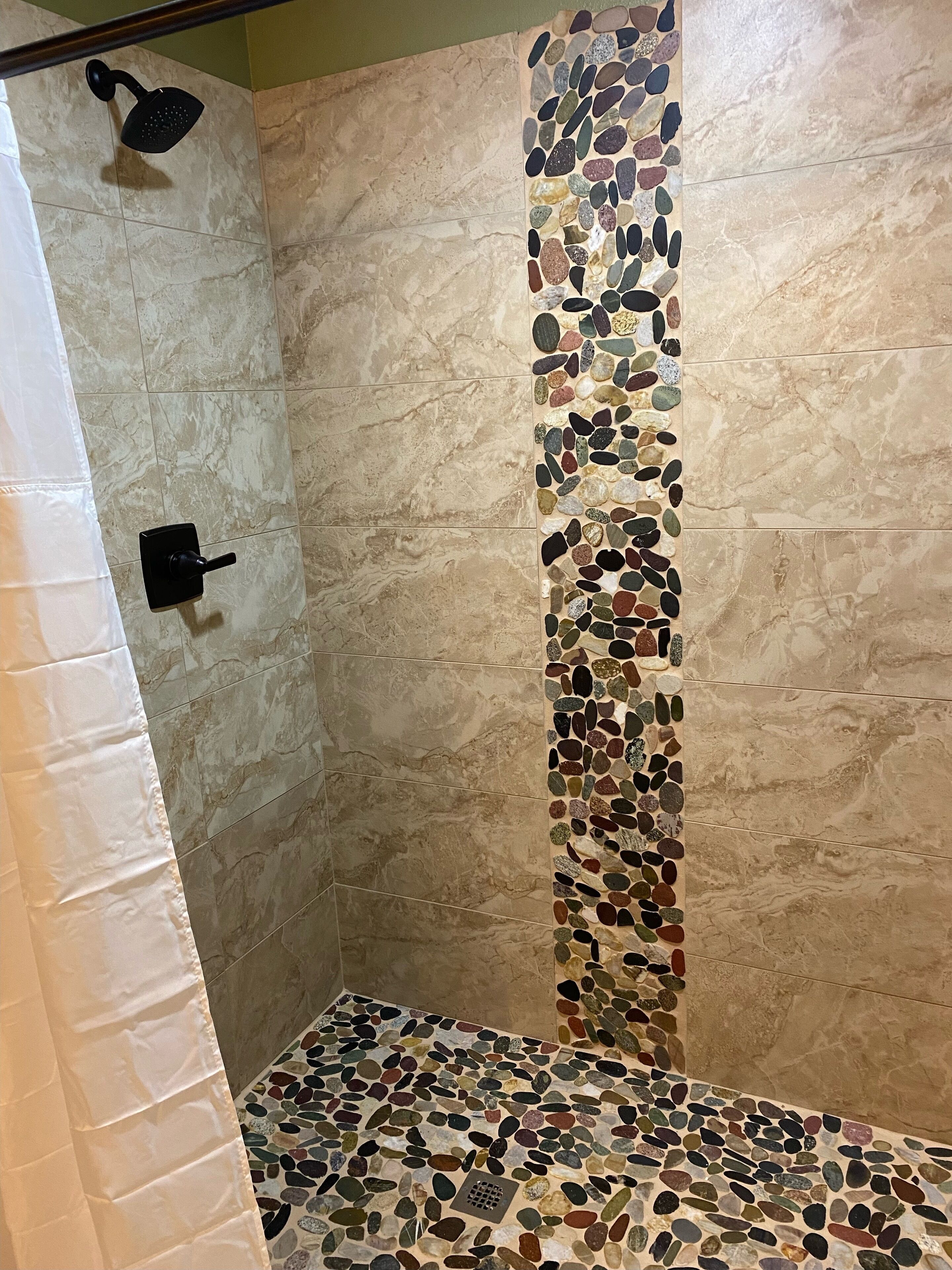 Une douche avec un bord en mosaïque de pierre et un pommeau de douche à main.