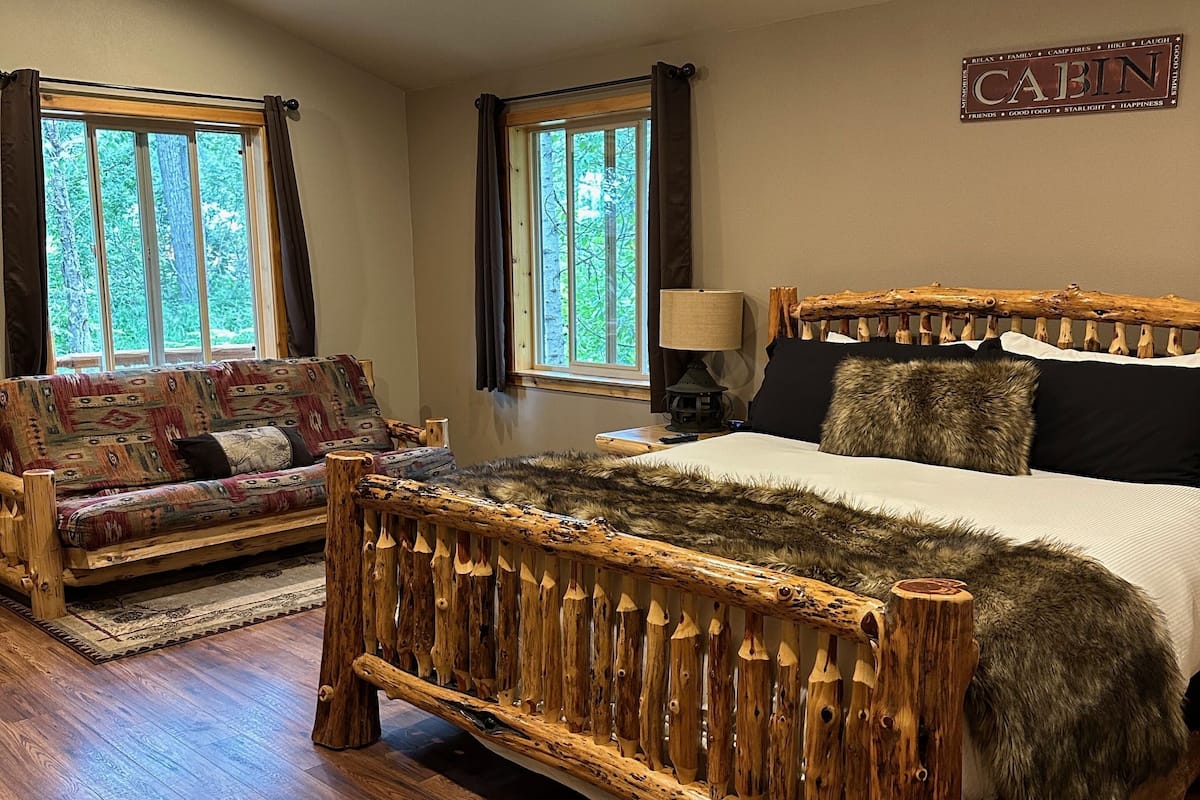 A bedroom with a wooden bed, a sofa, and two windows with curtains.