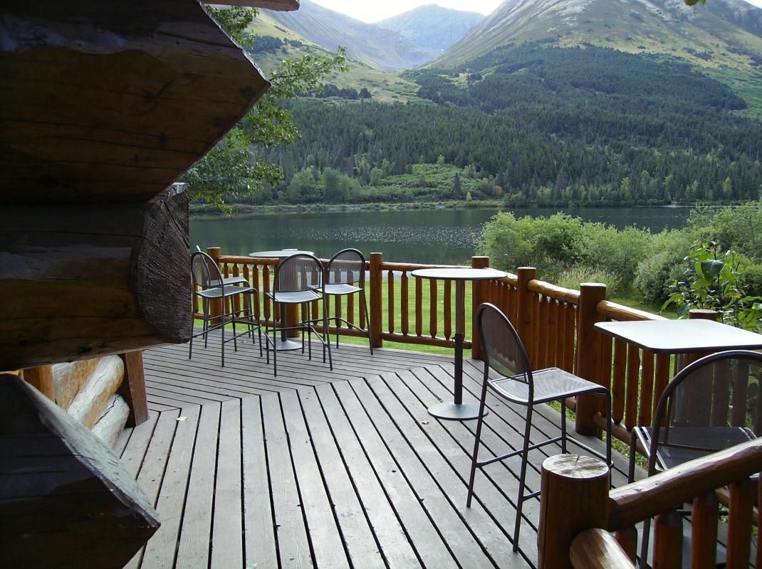 Une terrasse en bois avec des sièges extérieurs, offrant une vue sur un lac et des montagnes.