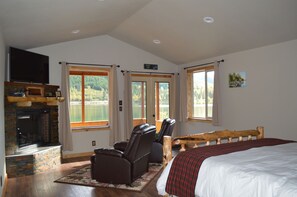 A bedroom with a large bed, a fireplace, a TV, and a view of a lake.