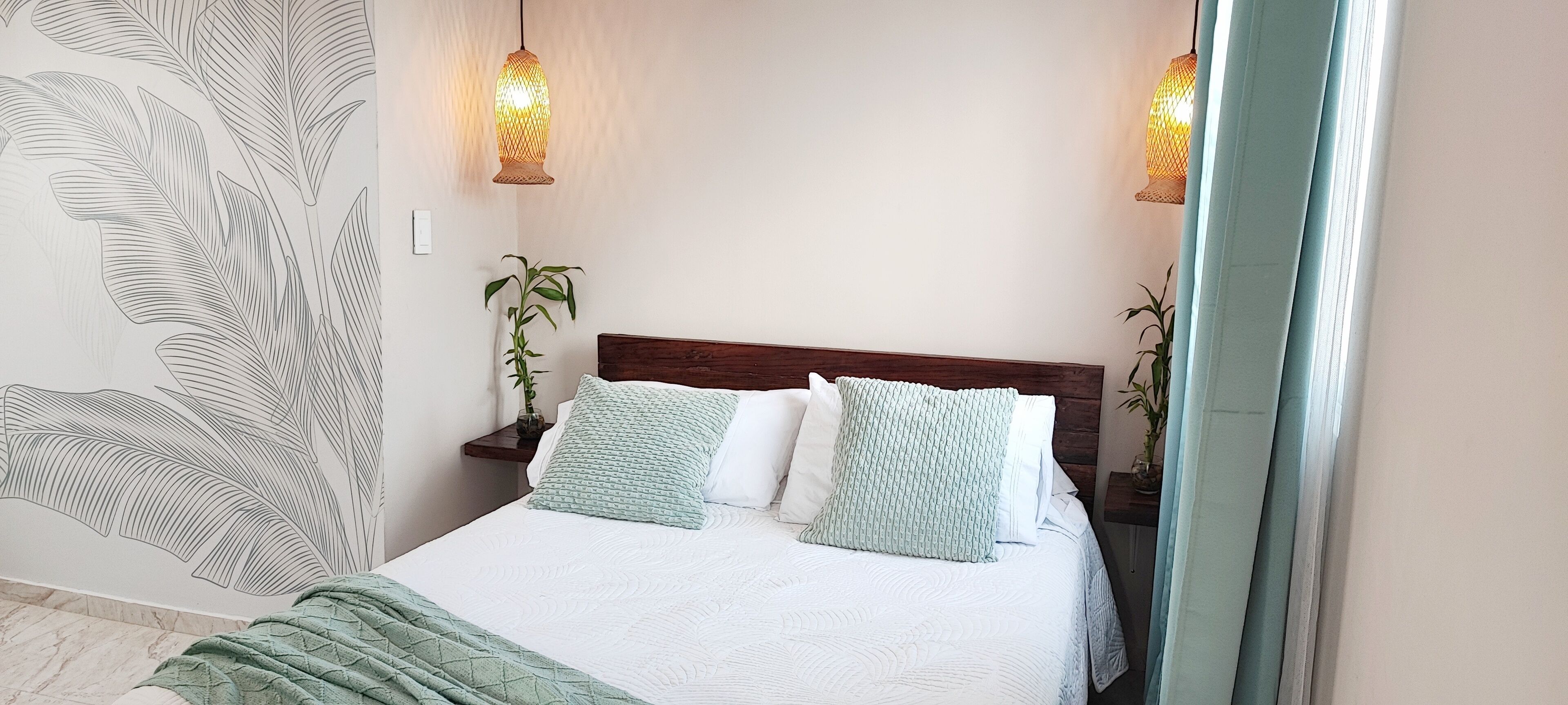 A bedroom with a bed, two bedside tables, a wall with a leaf pattern, and two wall-mounted lights.
