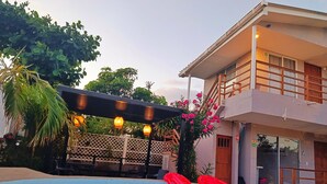 A swimming pool with inflatable rings, a covered area with hanging lights, and a two-story building with a balcony. - Cabañas Green Yard (San Andrés)