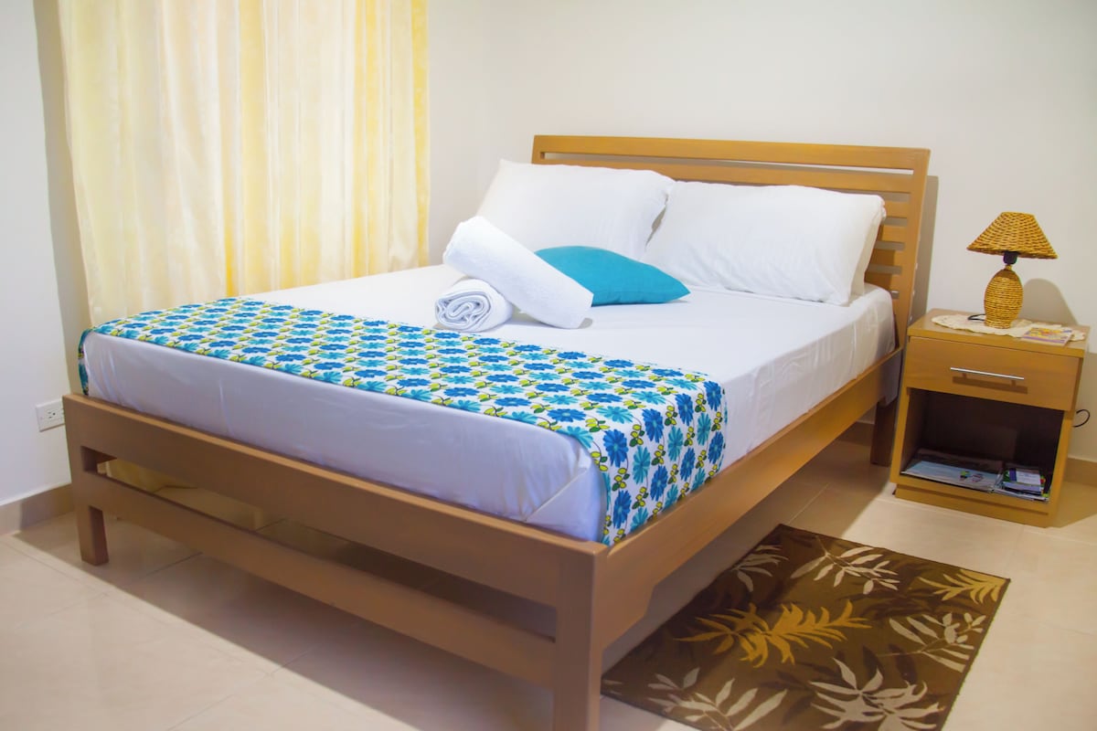 A neatly made bed with a patterned bedspread, a wooden headboard, and a bedside table with a lamp.