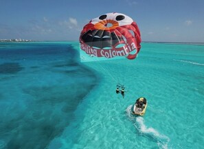 A parasailing activity over turquoise waters with a boat and a parasail labeled "Sailing Colombia". - Cabañas Green Yard (San Andrés)