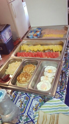 A buffet with various food items including pancakes, eggs, and fruits.