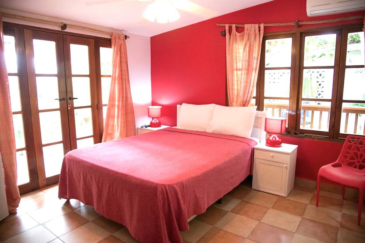 A bedroom with a bed, a nightstand, a chair, and a window with curtains.