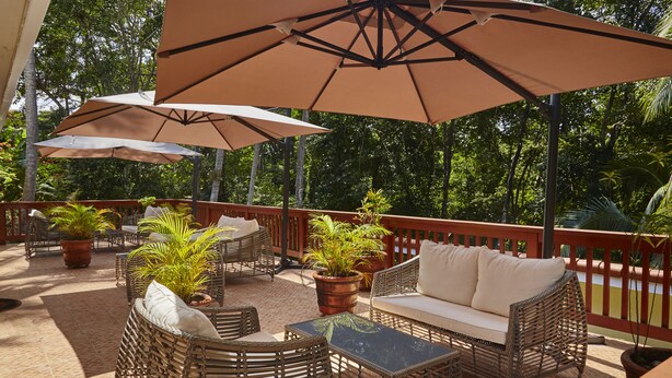 An outdoor patio with wicker furniture, potted plants, and large umbrellas.