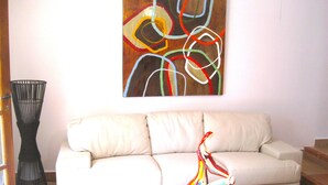 A living room with a white sofa, a glass coffee table, and a colorful abstract painting on the wall.