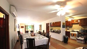 A dining area with a table set for six, a ceiling fan, and a kitchen in the background.