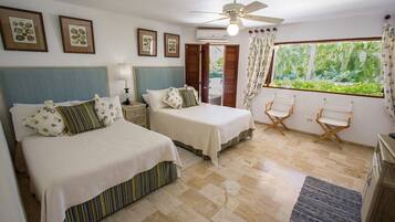A bedroom with two beds, a ceiling fan, a window with curtains, and a view of greenery outside.