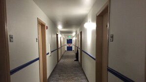 En lang, smal hotelgang med tæppebelagte gulve, blå paneler og døre med nummererede værelser.