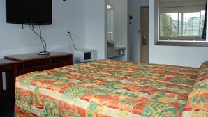Et hotelværelse med en seng, et skrivebord med tv og mikroovn, et vindue og en dør, der fører til et andet rum.