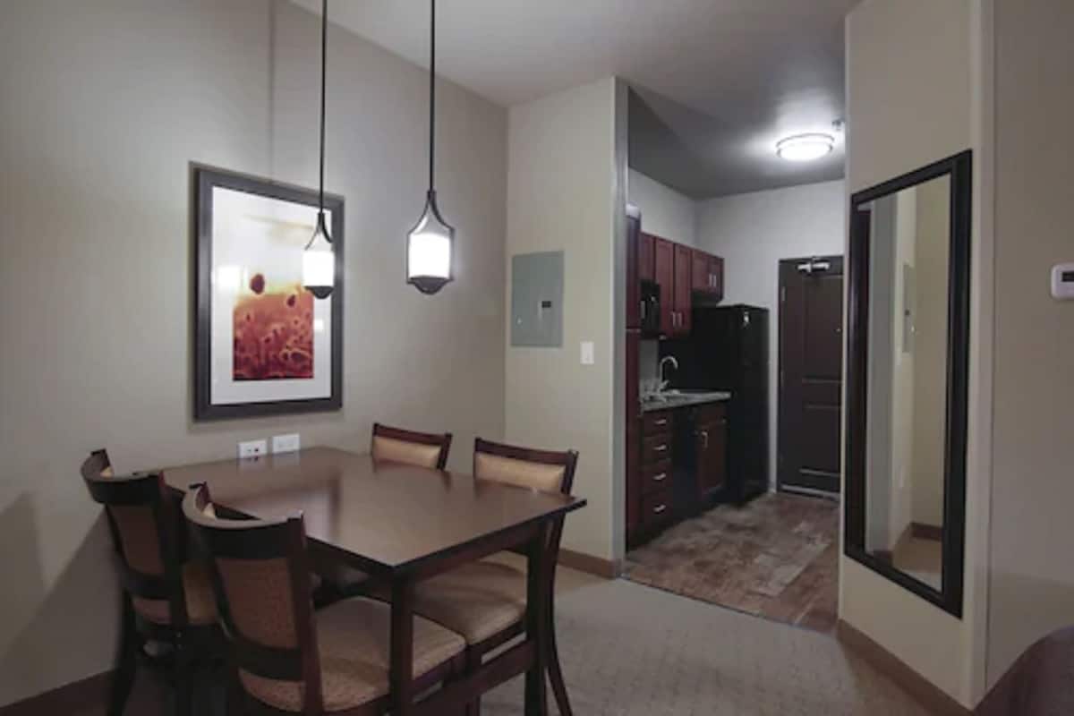 A dining area with a table and chairs, a kitchen with cabinets and appliances, and a mirror on the wall.