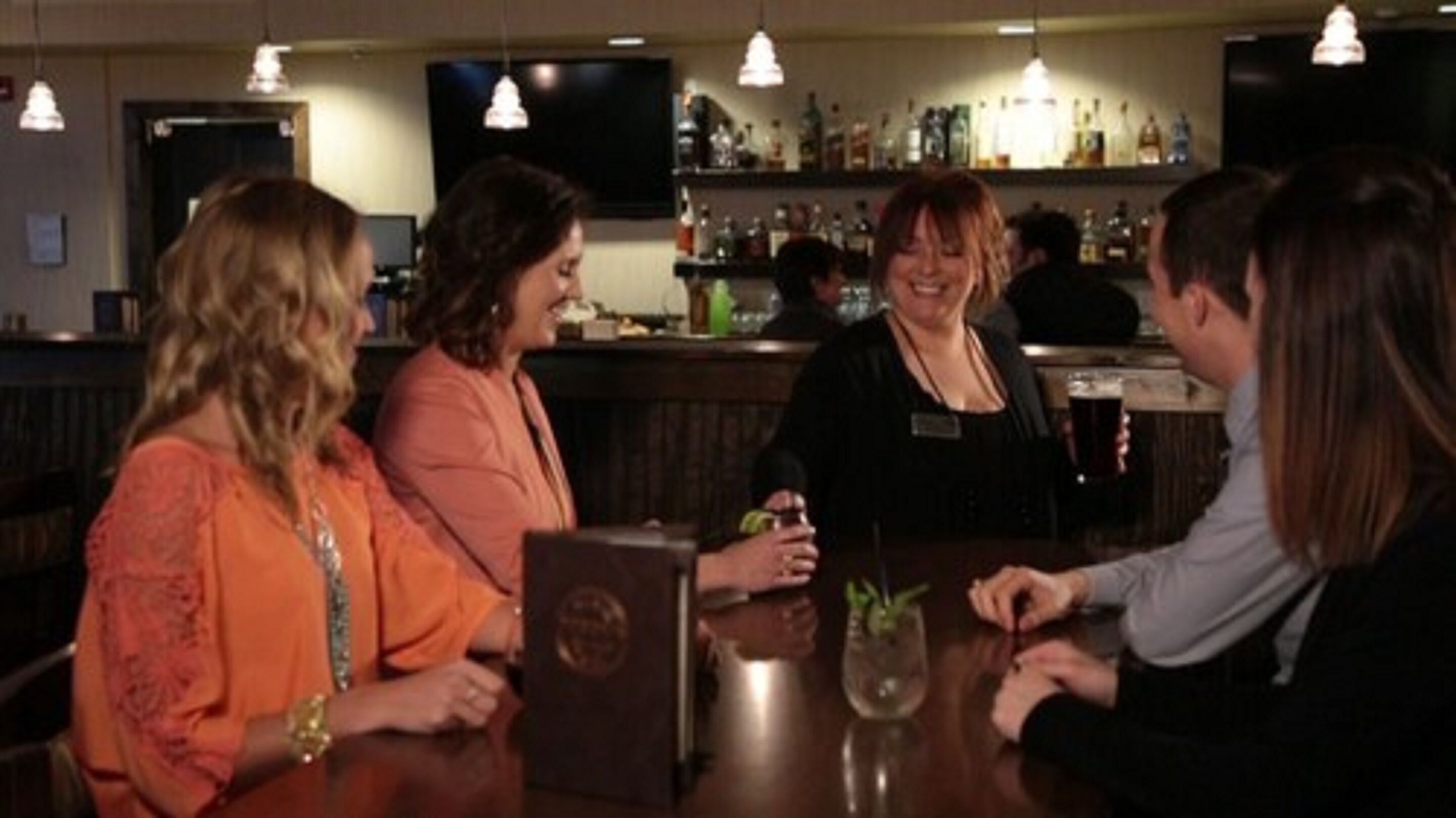 A bar area with a counter, bottles, and a television screen.