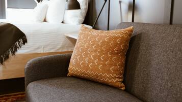 A modern hotel room with a grey sofa, a patterned throw pillow, and a neatly made bed with white linens.