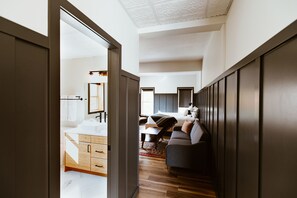 A modern hotel room with a wooden floor, a sofa, a bed, and a bathroom with a sink and mirror. - The Flying Steamshovel Inn (Rossland)