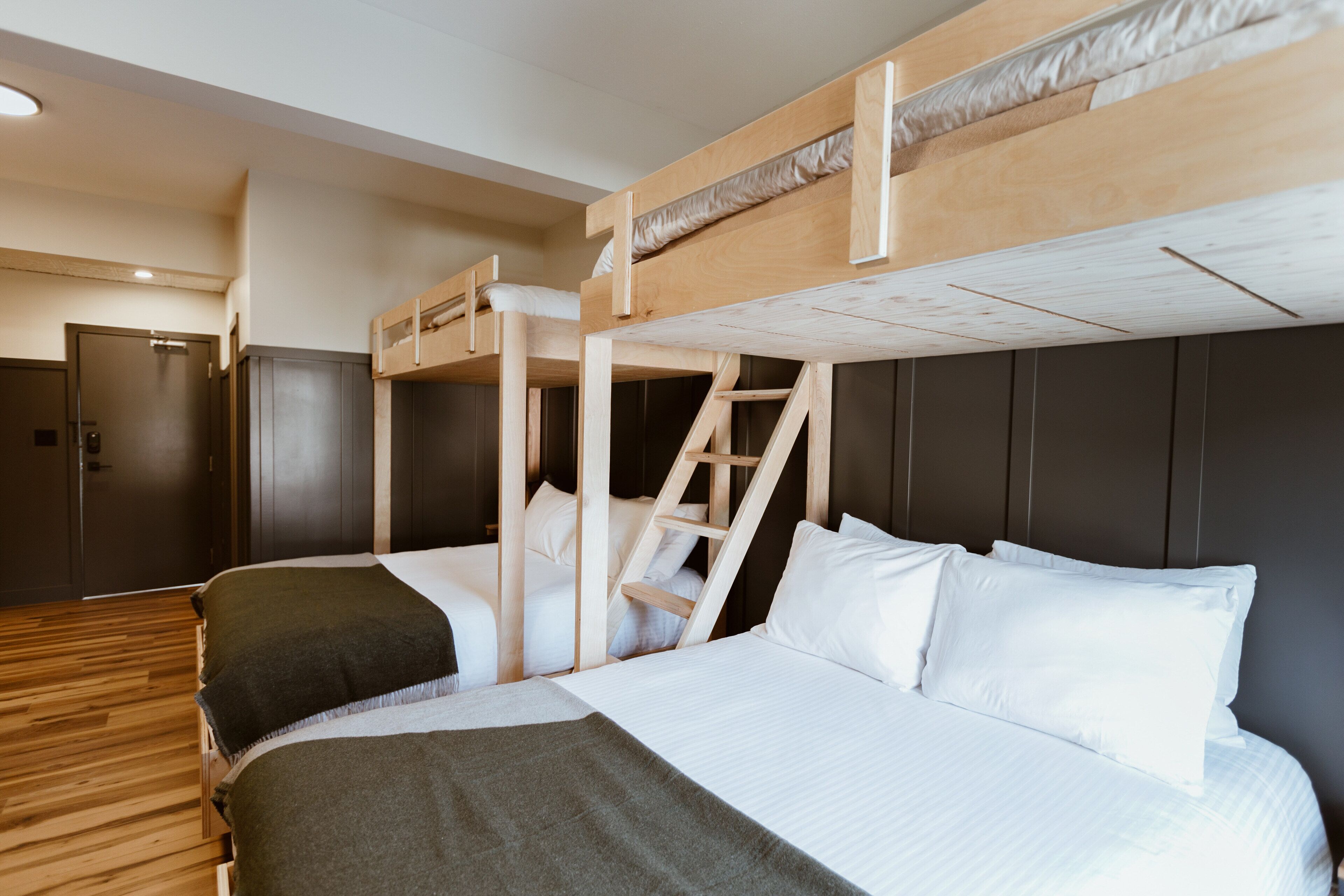 A bunk bed room with a wooden ladder, a door, and a wooden floor.