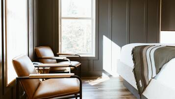 Ein modernes Schlafzimmer mit einem großen Fenster, einem Bett mit gestreifter Decke, zwei Ledersesseln und einem gemusterten Teppich.
