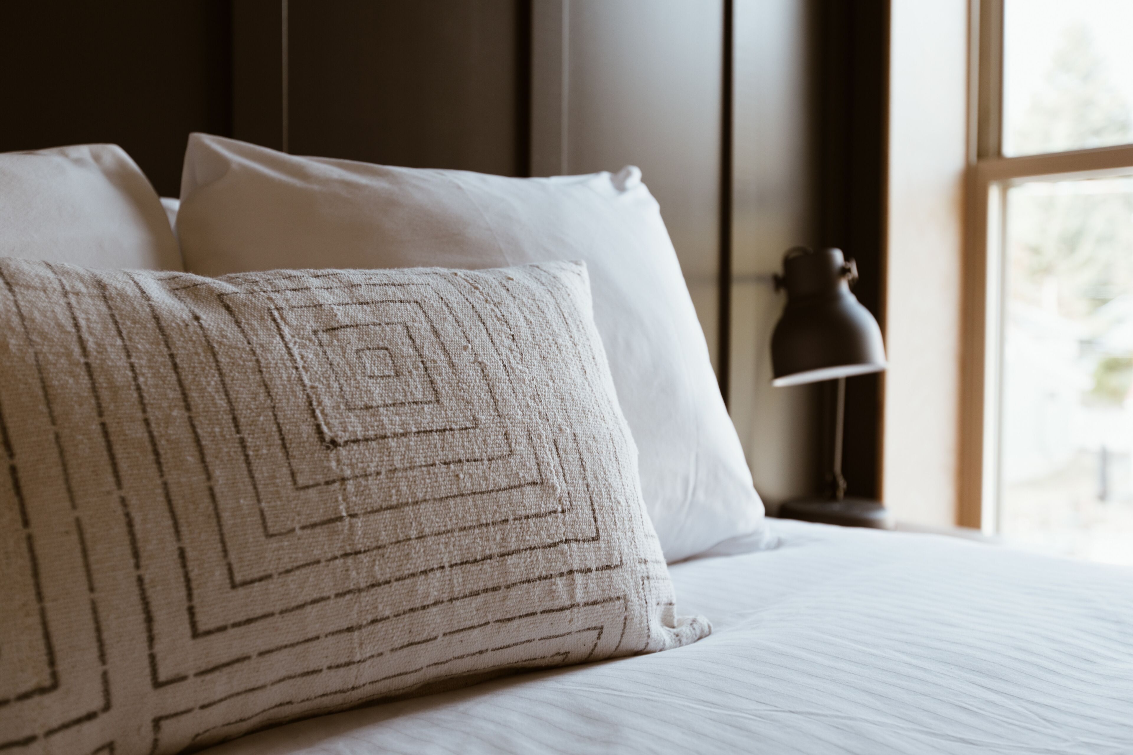 A neatly made bed with white linens and a patterned pillow.