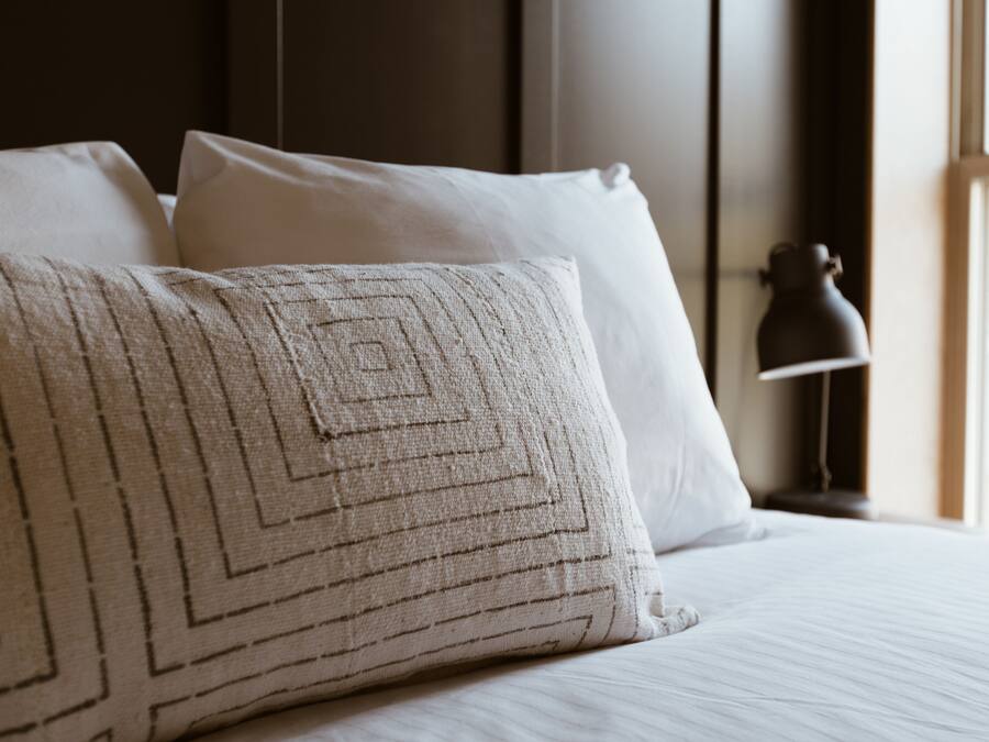 A neatly made bed with white linens and a patterned pillow.