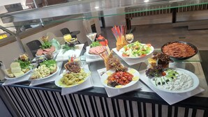 Ein Buffet mit verschiedenen Speisen, darunter Salate, Fleischgerichte und Desserts.