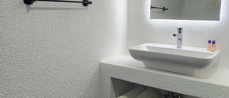 A bathroom with a white textured wall, a black towel rack, a white sink with a mirror, and dark tiled flooring.