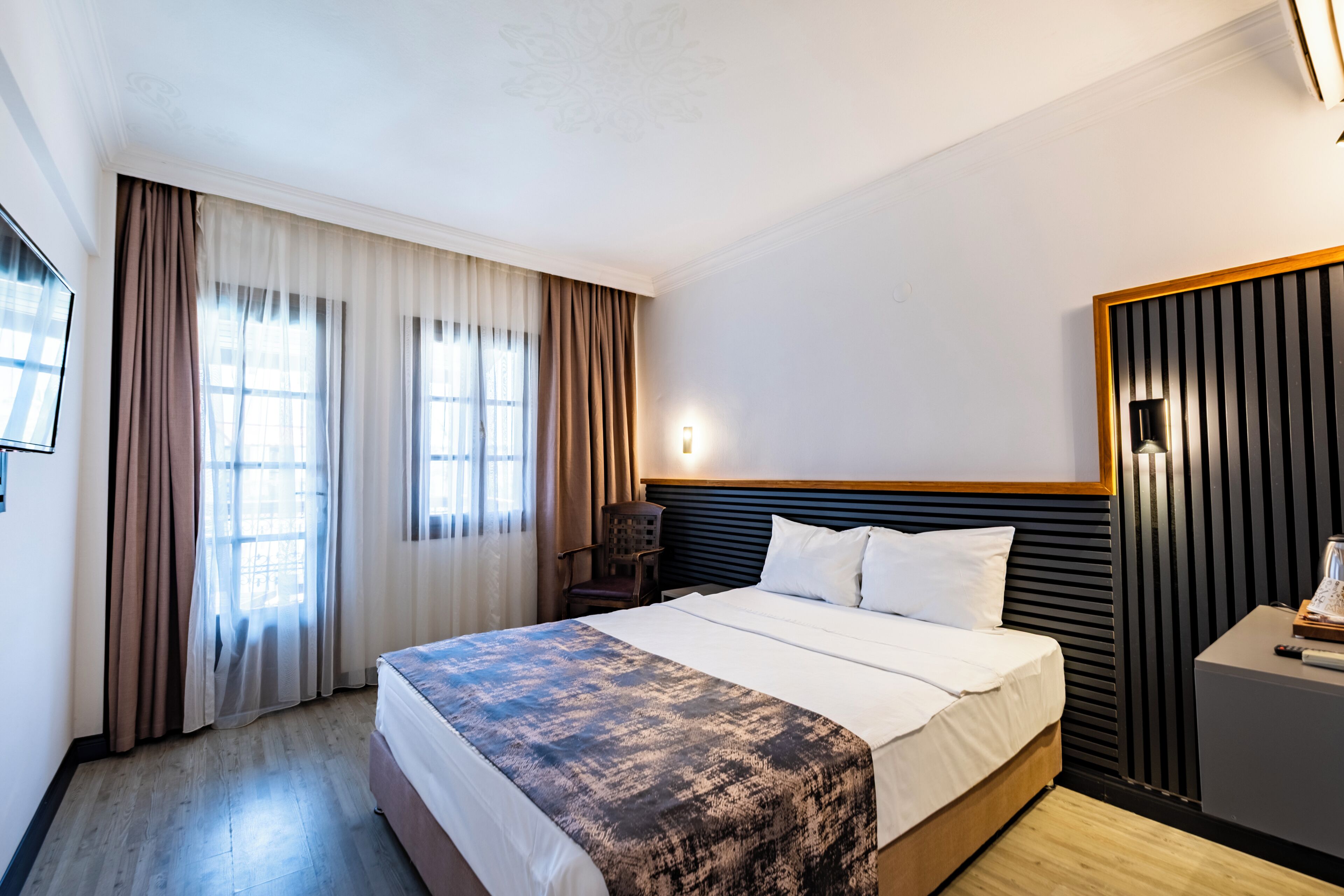 A hotel room with a bed, a nightstand, a lamp, a chair, and a window with curtains.