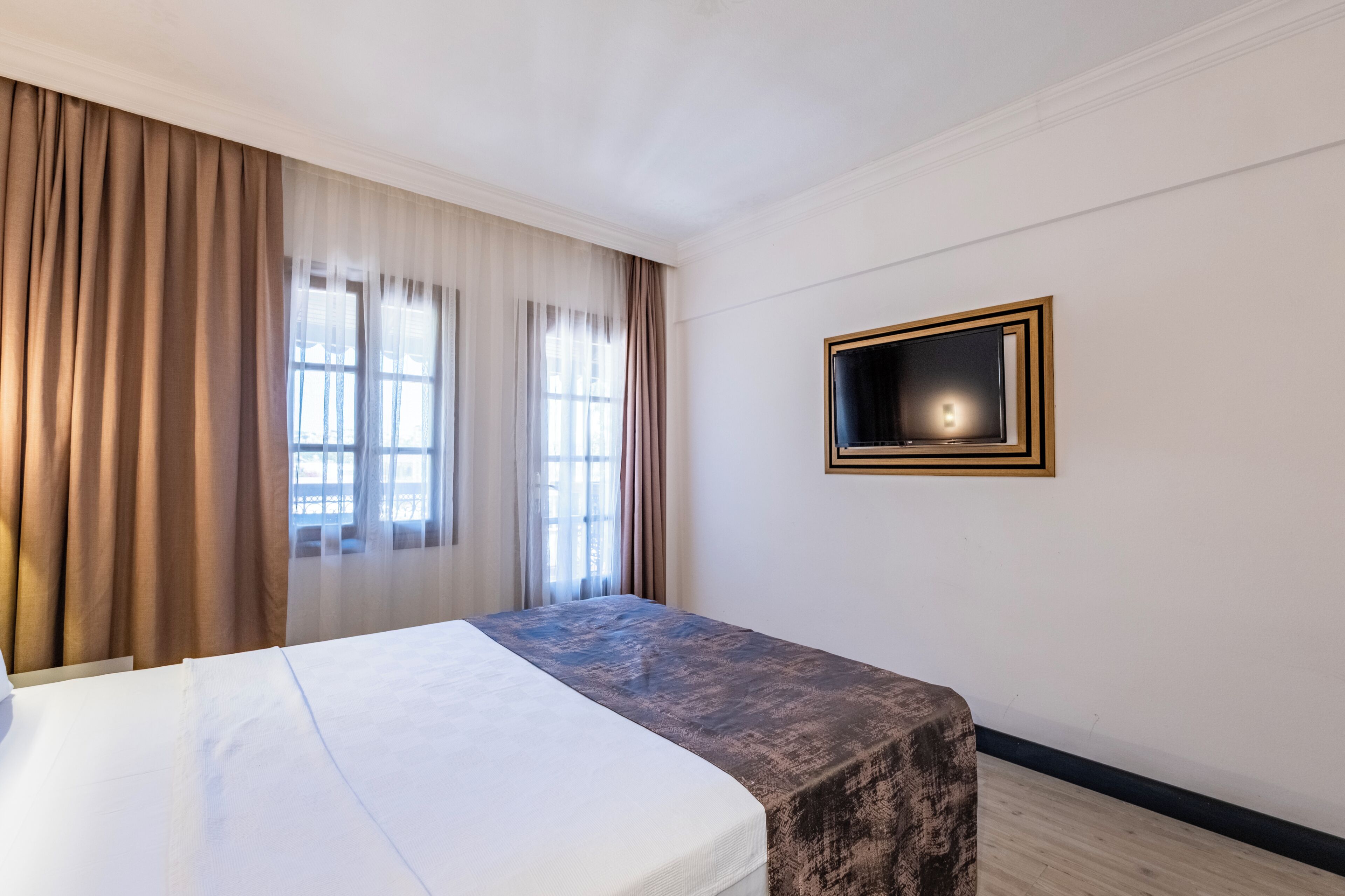 Una habitación de hotel con una cama, una mesita de noche, una ventana con cortinas y un televisor montado en la pared.
