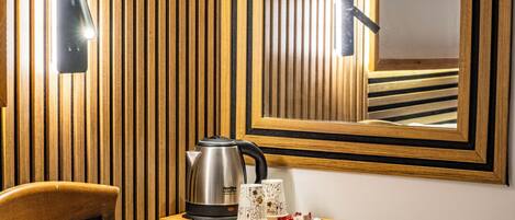 A wooden-paneled wall with a kettle, two mugs, a tray with items, a remote control, and a mirror reflecting the room.