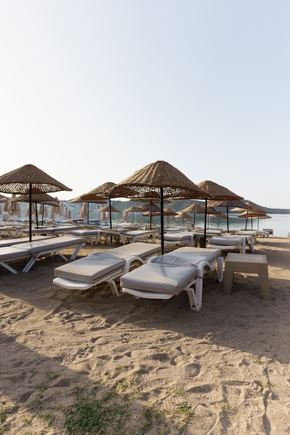 A beach with rows of sun loungers and thatched umbrellas.
