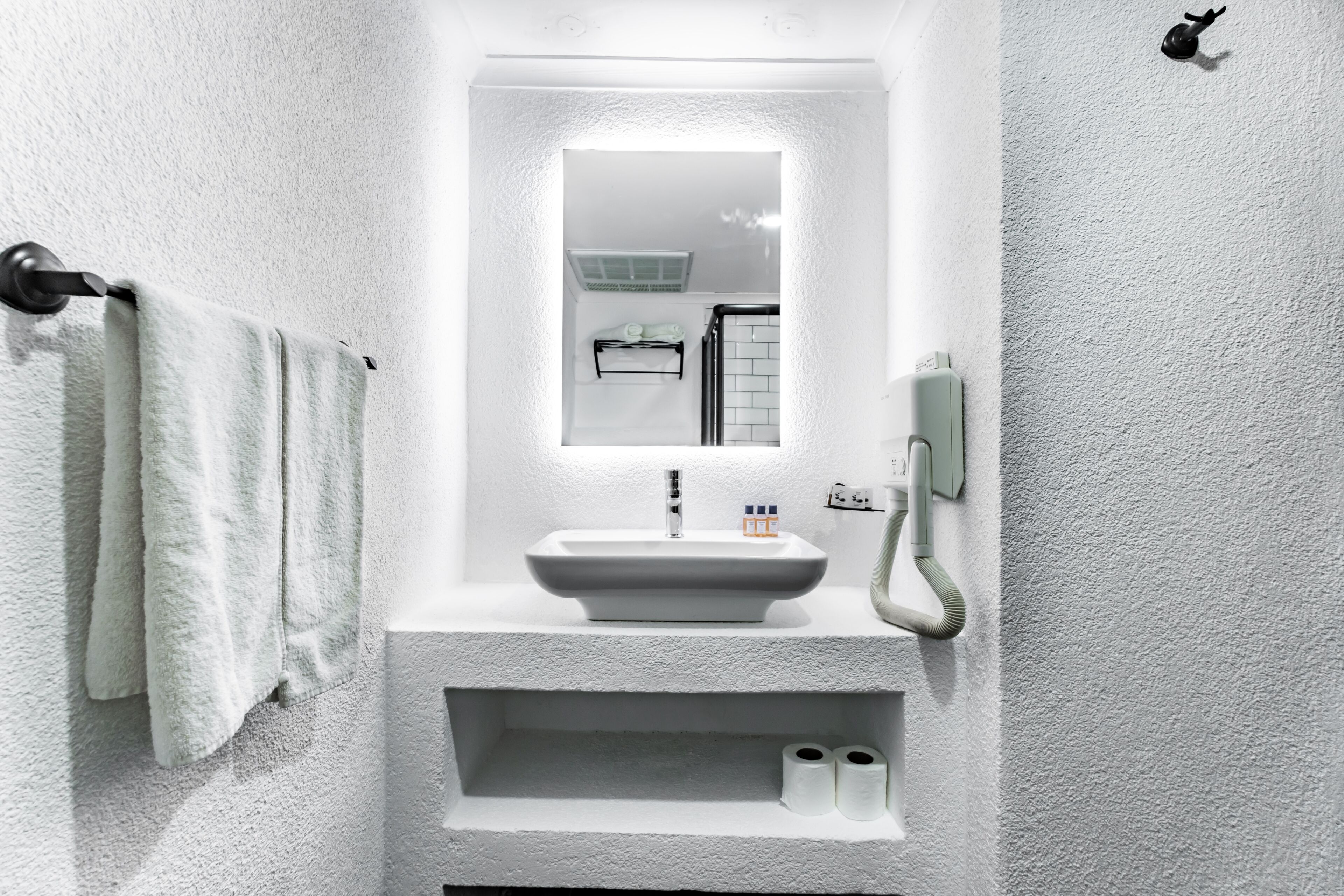 Une salle de bain avec un lavabo blanc, un miroir, un porte-serviettes et un sèche-mains.