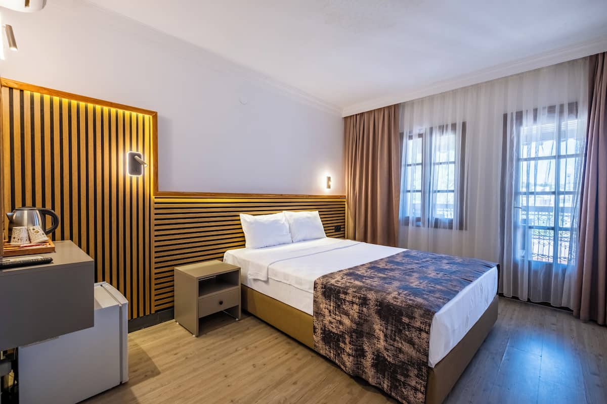 Une chambre d’hôtel avec un lit, une table de chevet, une lampe, des rideaux et une fenêtre donnant sur un paysage agréable.