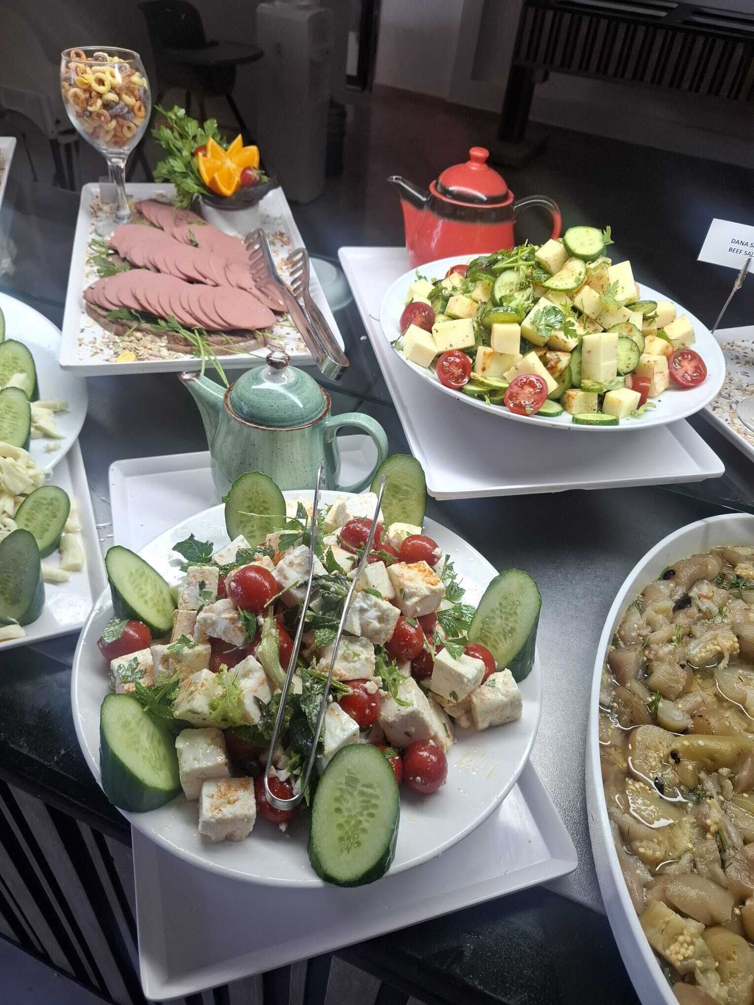 A buffet with various dishes including a salad with cucumbers and tomatoes, a dish with cubes of cheese and cucumbers, and a plate with sliced meat.