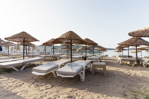 A beach with rows of sun loungers and thatched umbrellas, arranged in a linear fashion along the shoreline. - Costa Bitezhan Hotel (Bodrum)