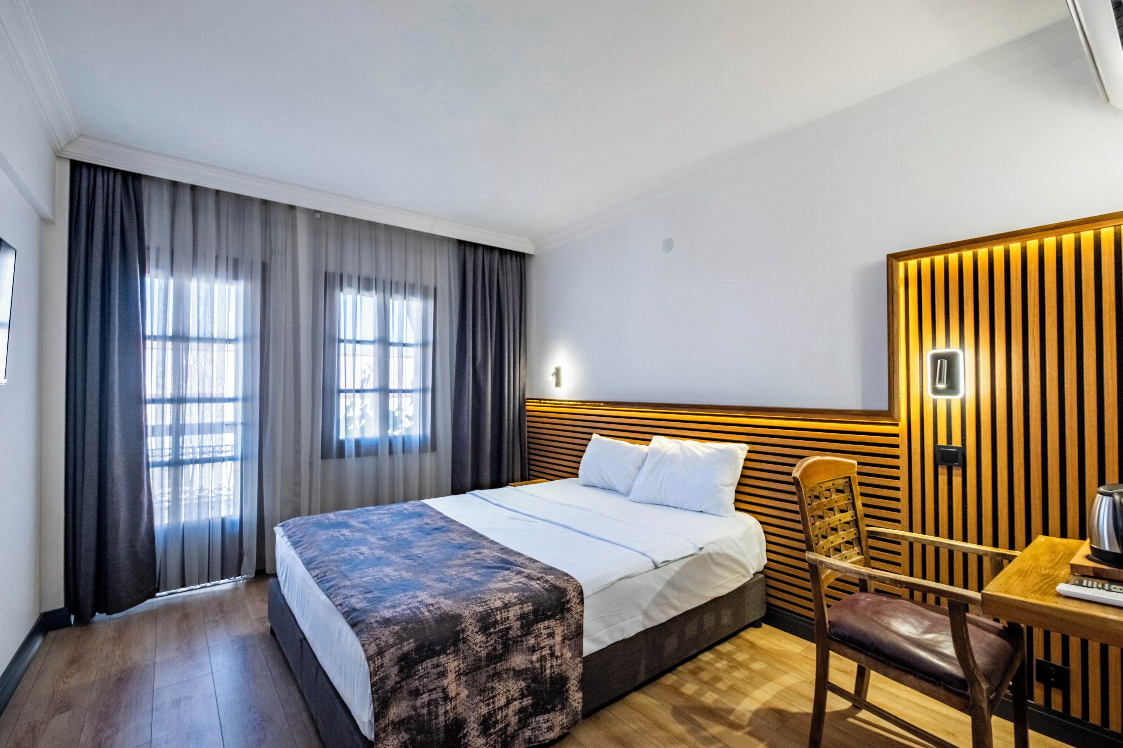 A hotel room with a bed, a desk, a chair, and a wall-mounted light fixture.