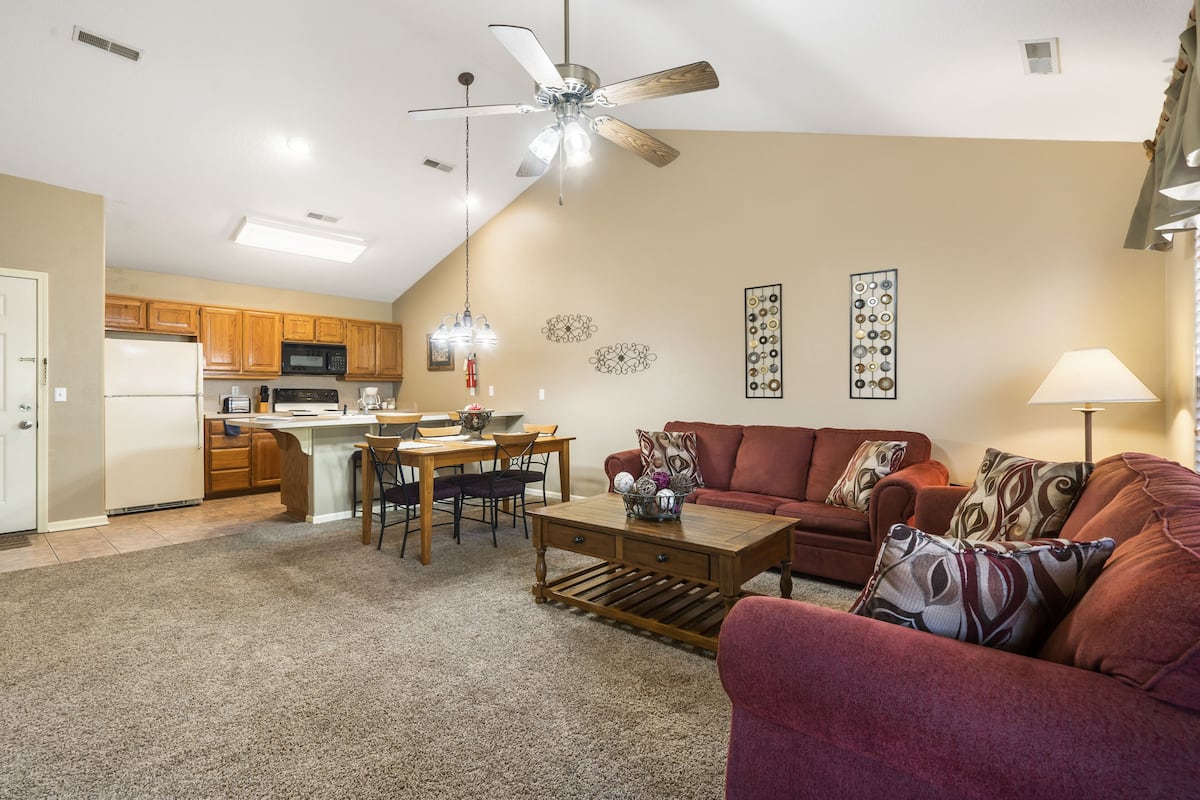 A spacious living room with a red couch, a coffee table, and a dining area with a kitchen in the background.