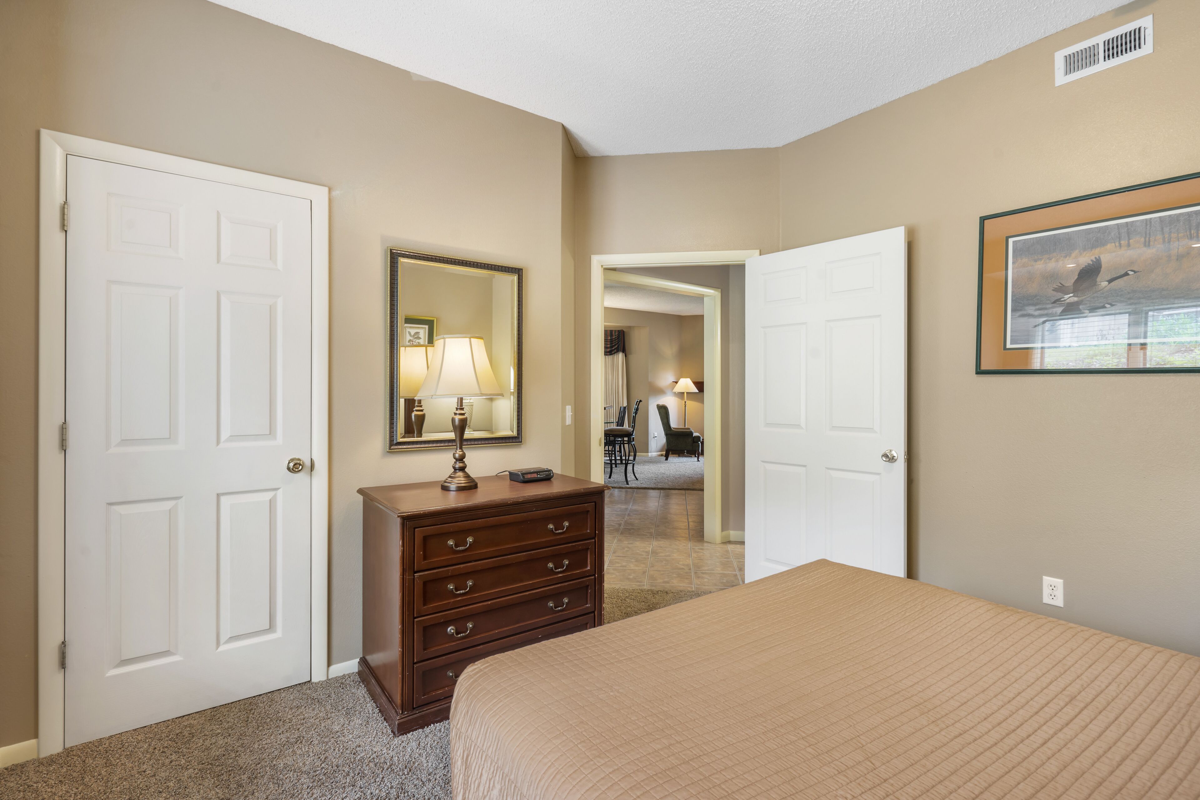 A hotel room with a bed, a dresser, a mirror, and a door leading to another room.